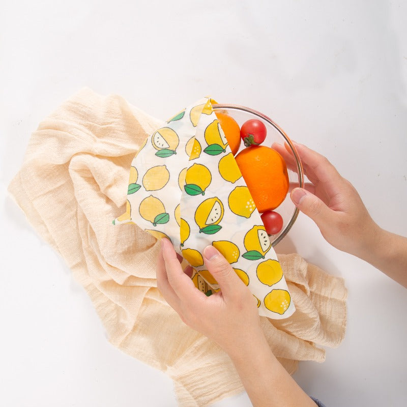 Reusable beeswax food wrap with lemon and citrus pattern, secured around a bowl