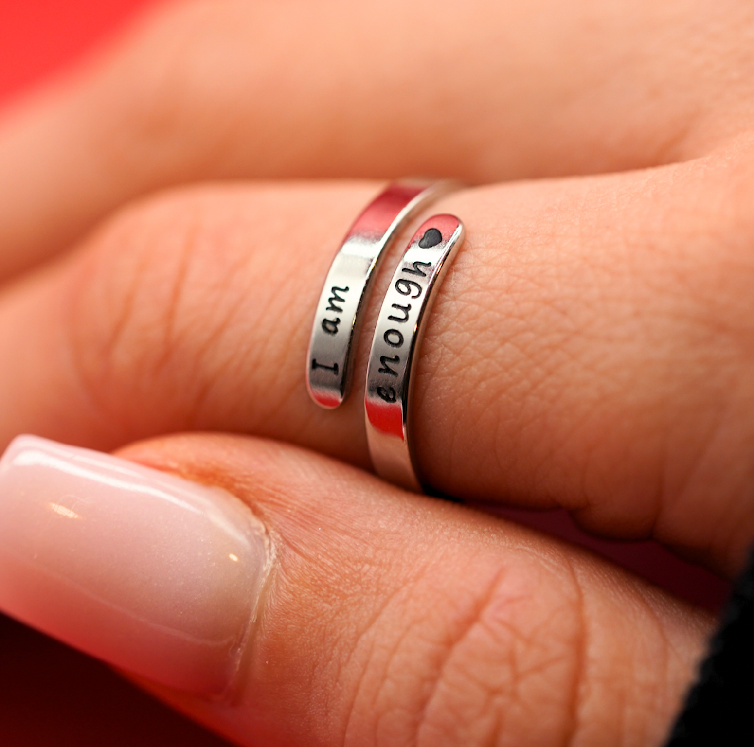 Silver ring with “I am enough” engraving and red inner lettering, close-up
