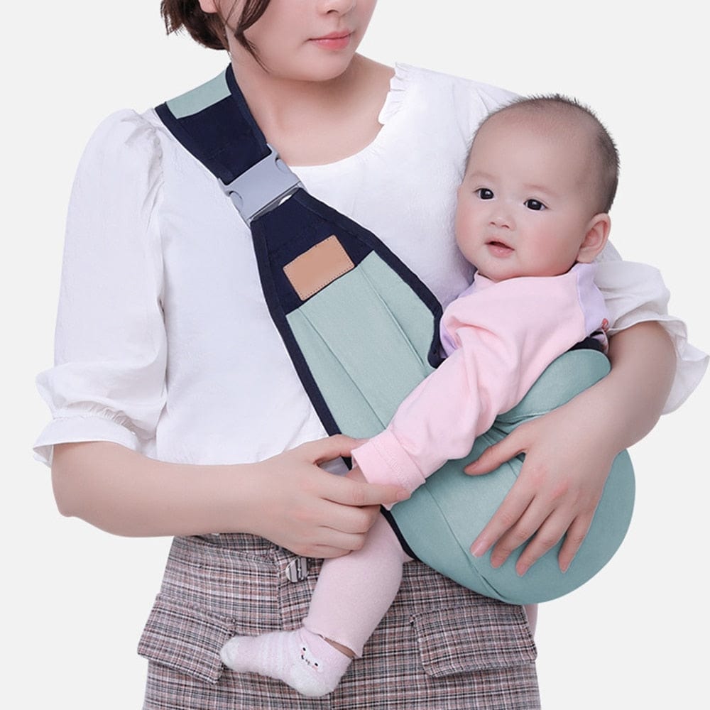 Adjustable baby shoulder carrier sling with green pouch and navy straps, holding a baby.