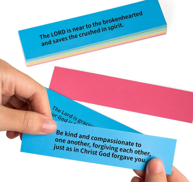 Hand holding folded Bible verse cards in bright blue and pink with scripture quotes