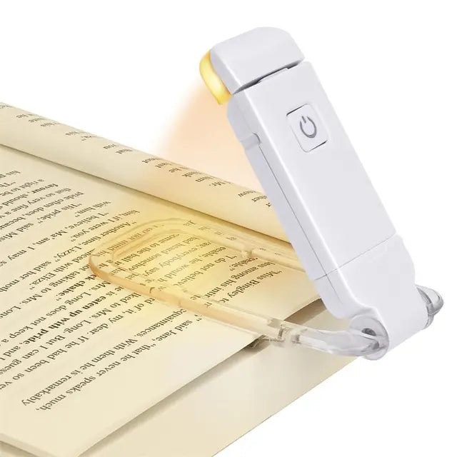 White clip-on LED book light with clear clamp, resting on an open book