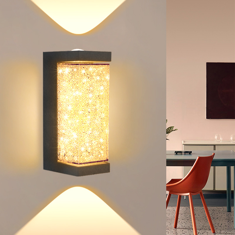 Square LED wall sconce with speckled amber glass cylinder and black frame, lit