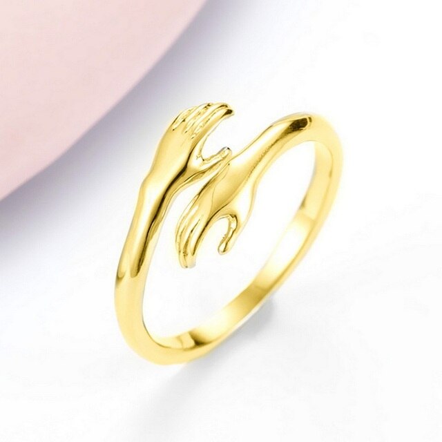 Gold-tone ring with raised hand design and heart cutout, angled view