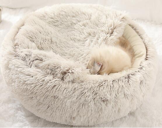 Cream plush pet bed with raised rim and tunnel entrance, small dog sleeping inside.