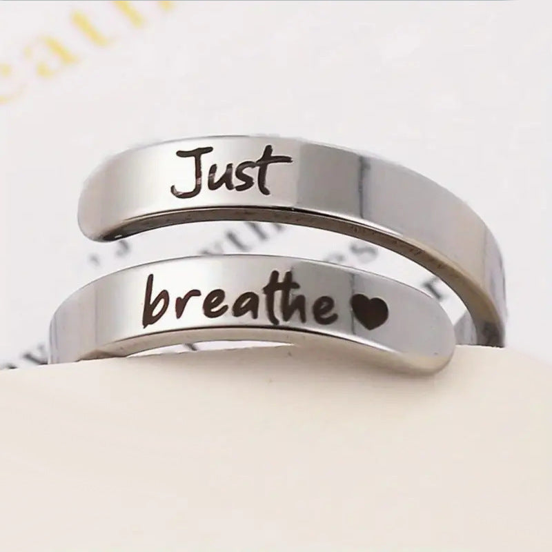 Silver engraved ring showing "Just" and "breathe" with heart icon detail