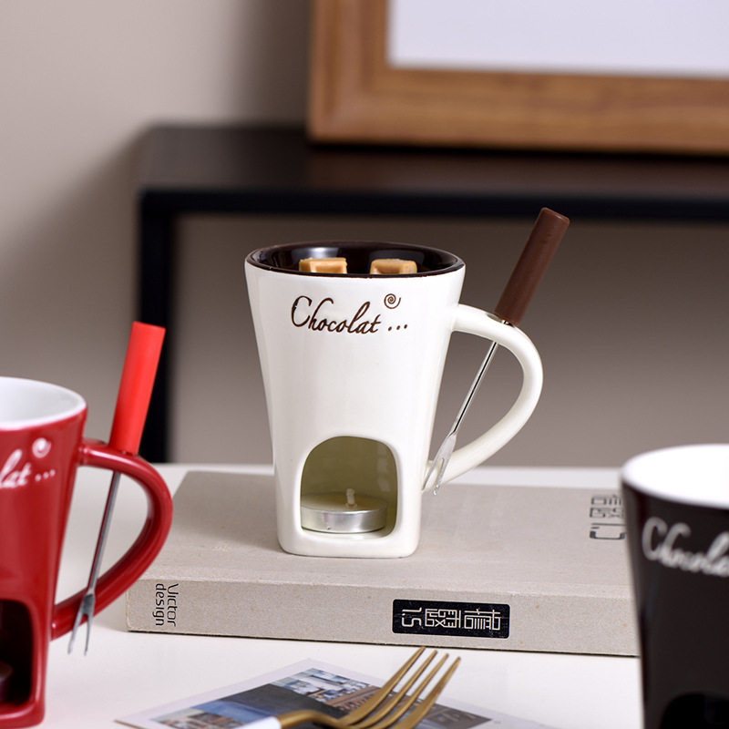 White mini fondue mug with wooden handle, lit warmer, and metal fork on stand