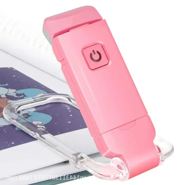 Pink clip-on LED book light with clear clamp, angled on an open book
