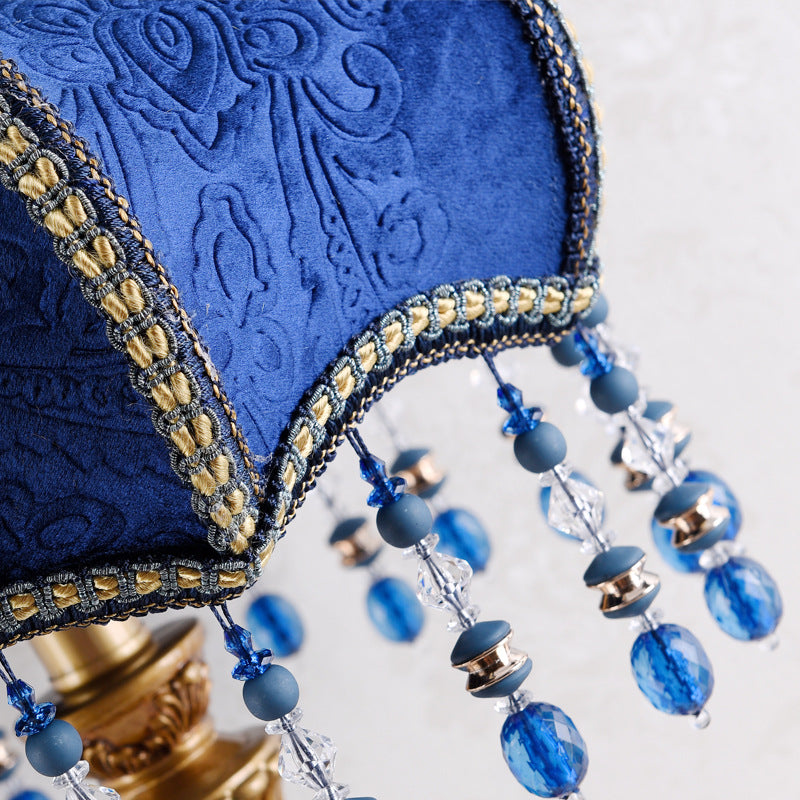 Blue fabric lamp shade with ornate trim and hanging crystal and blue bead fringe