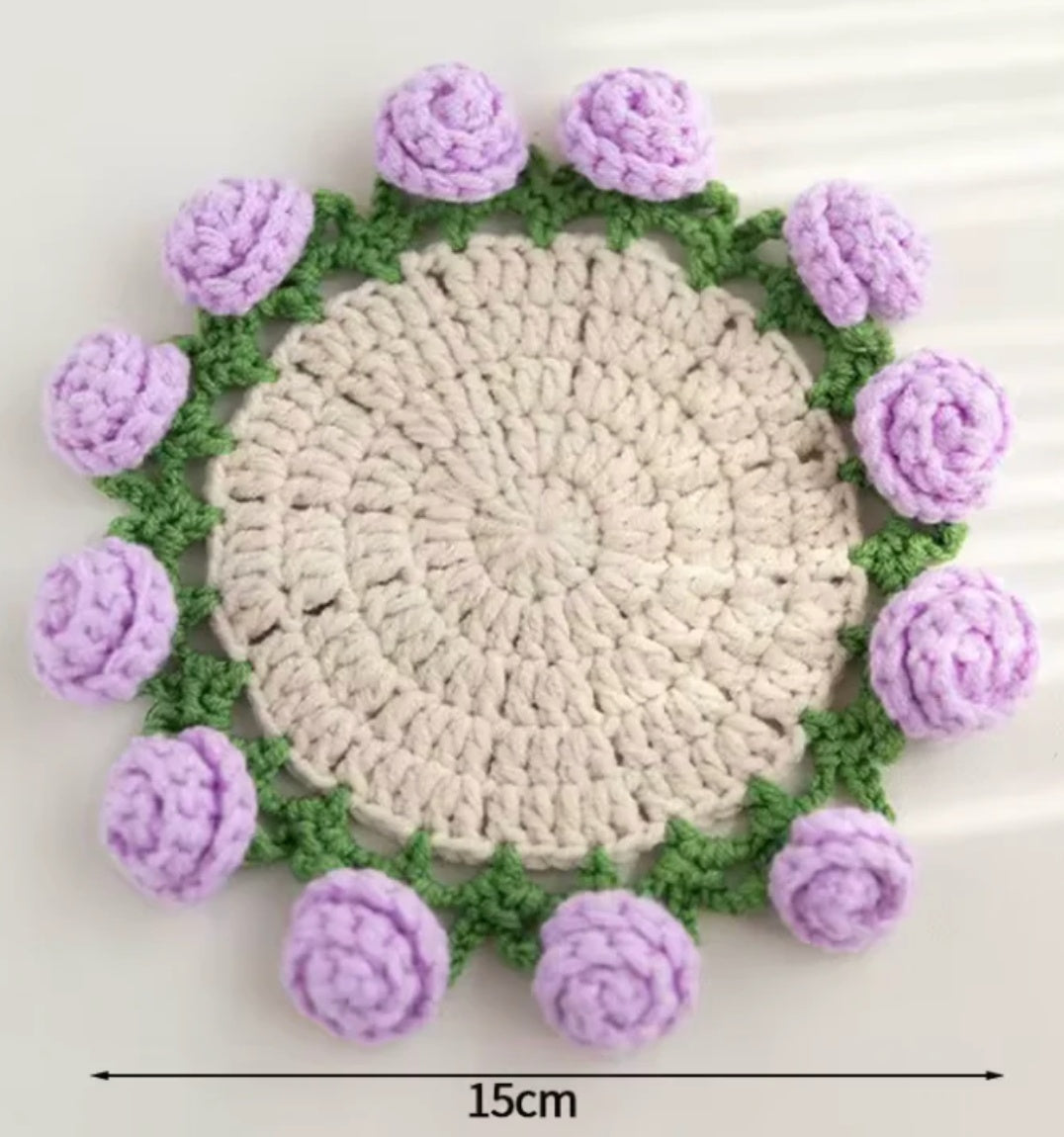 Crochet coaster with cream center, green border, and purple rose bud accents