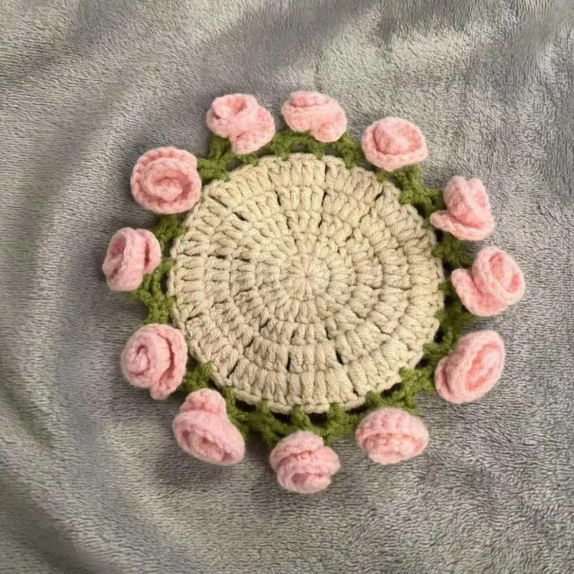 Crochet coaster with beige center, green leafy ring, and pink rose appliques