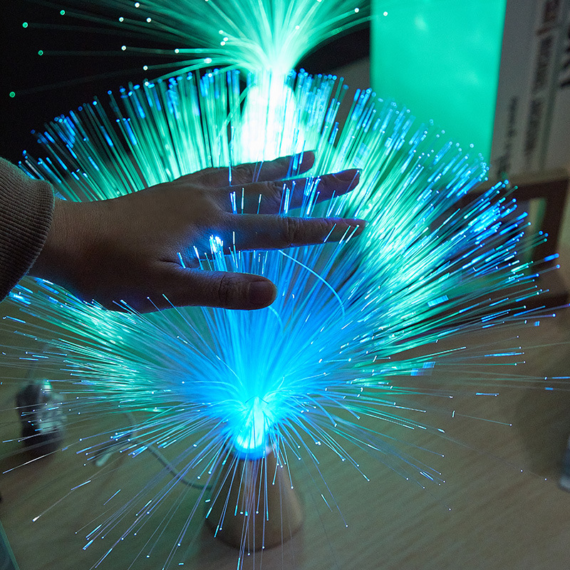 Fiber optic colour-changing lamp glowing green and blue, with hand touching fiber strands