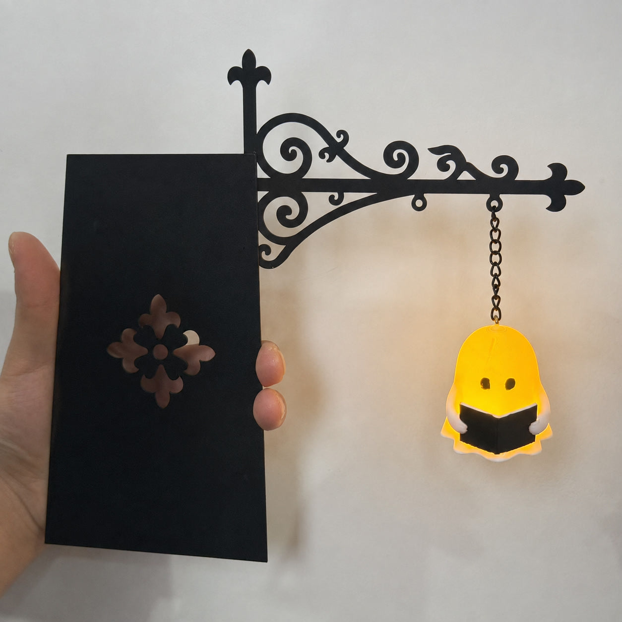 Black metal shelf ornament with hanging yellow ghost silhouette on chain