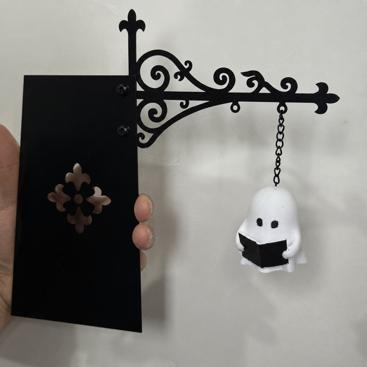 Black metal shelf ornament with hanging white ghost silhouette and chain