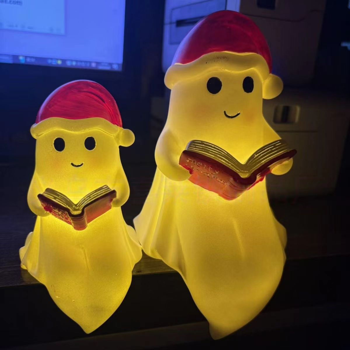Two reading ghost night lights with red caps, each holding an open book