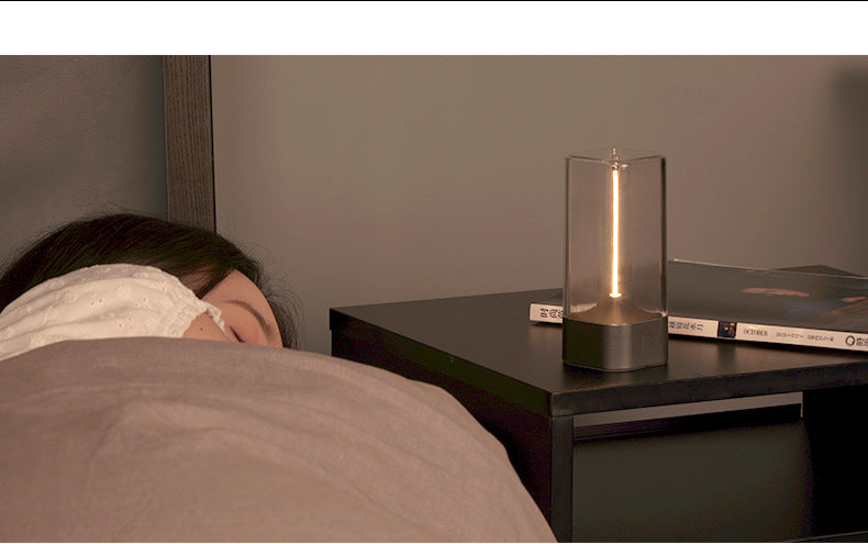 Portable LED night light on tabletop, clear glass cylinder with warm glow and dark base