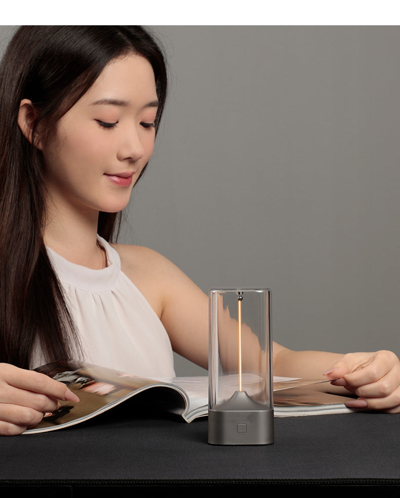 Portable LED night light on desk, clear glass cylinder with warm glow and dark base