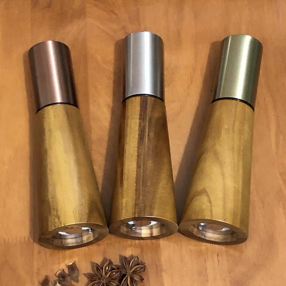 Acacia wood pepper and salt grinders with metal caps in three finishes on a wooden board