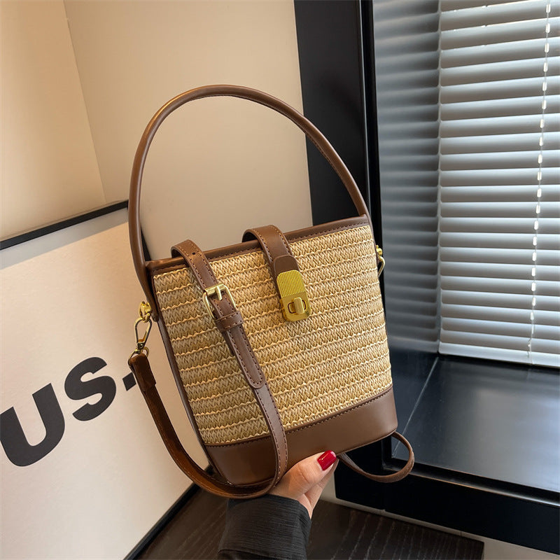 Woven straw bucket bag with tan leather trim, top handle, and crossbody strap.