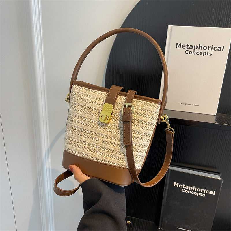 Woven straw bucket bag with tan leather straps, gold buckle detail, and crossbody strap.