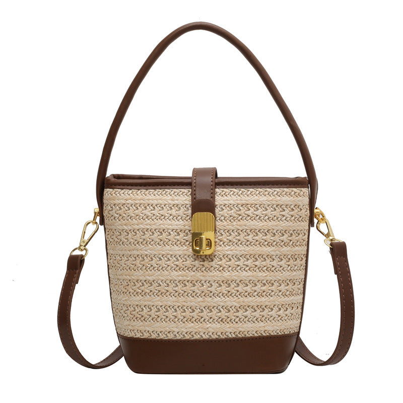 Light beige woven bucket bag with brown leather bottom, top handle, and crossbody straps.