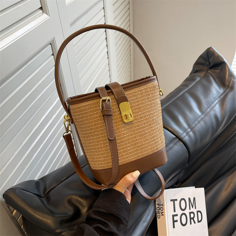 Woven straw bucket bag with brown leather front strap and top handle, with crossbody strap.