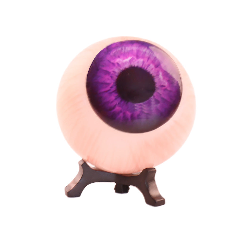 Close-up resin purple eyeball ornament with violet iris and dark pupil on black stand