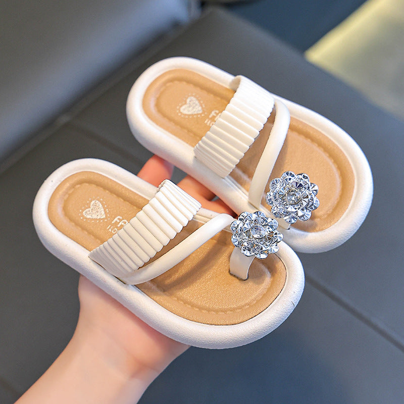 Girls' flip-flops held in hand, white straps with ribbed texture and rhinestone flower details