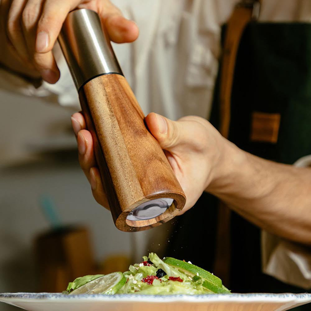 Acacia wood pepper grinder being held above plated salad with visible grinding opening