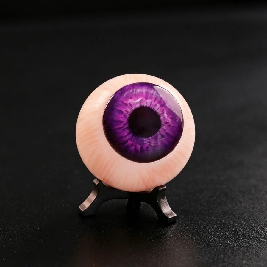 Resin purple eyeball ornament with dark pupil and violet iris on black tripod base