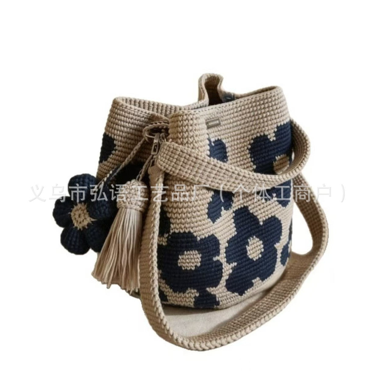 Beige crochet tote bag with dark blue floral pattern, pom flowers, and tassel charm