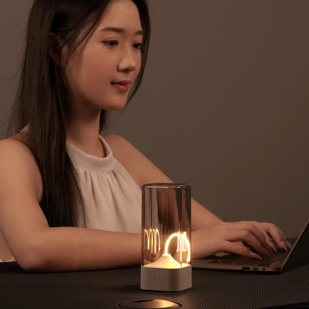 Portable LED night light on desk, clear glass cylinder with warm glow and dark base