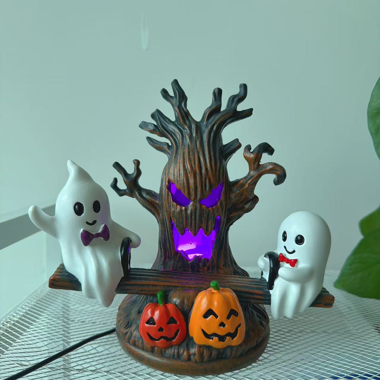 Swing ghost night light on tabletop with purple glowing haunted tree, two ghosts, and pumpkins