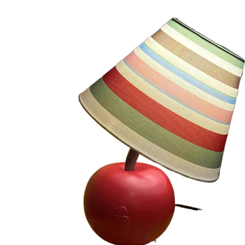 Apple-shaped bedside lamp with red apple base and multi-color striped shade, angled.