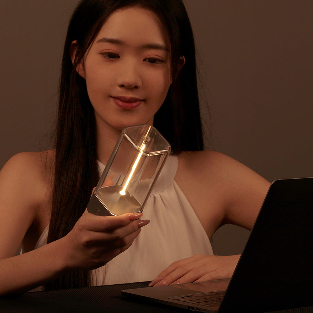 Portable LED night light in hand, clear glass cylinder with warm glow and dark base