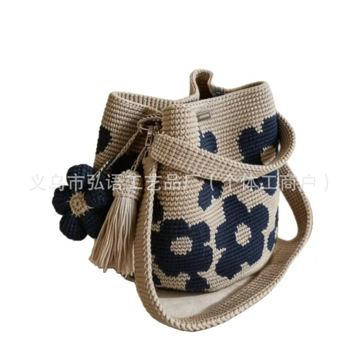 Beige crochet tote bag with dark blue flower patches, pom flowers, and tassel trim