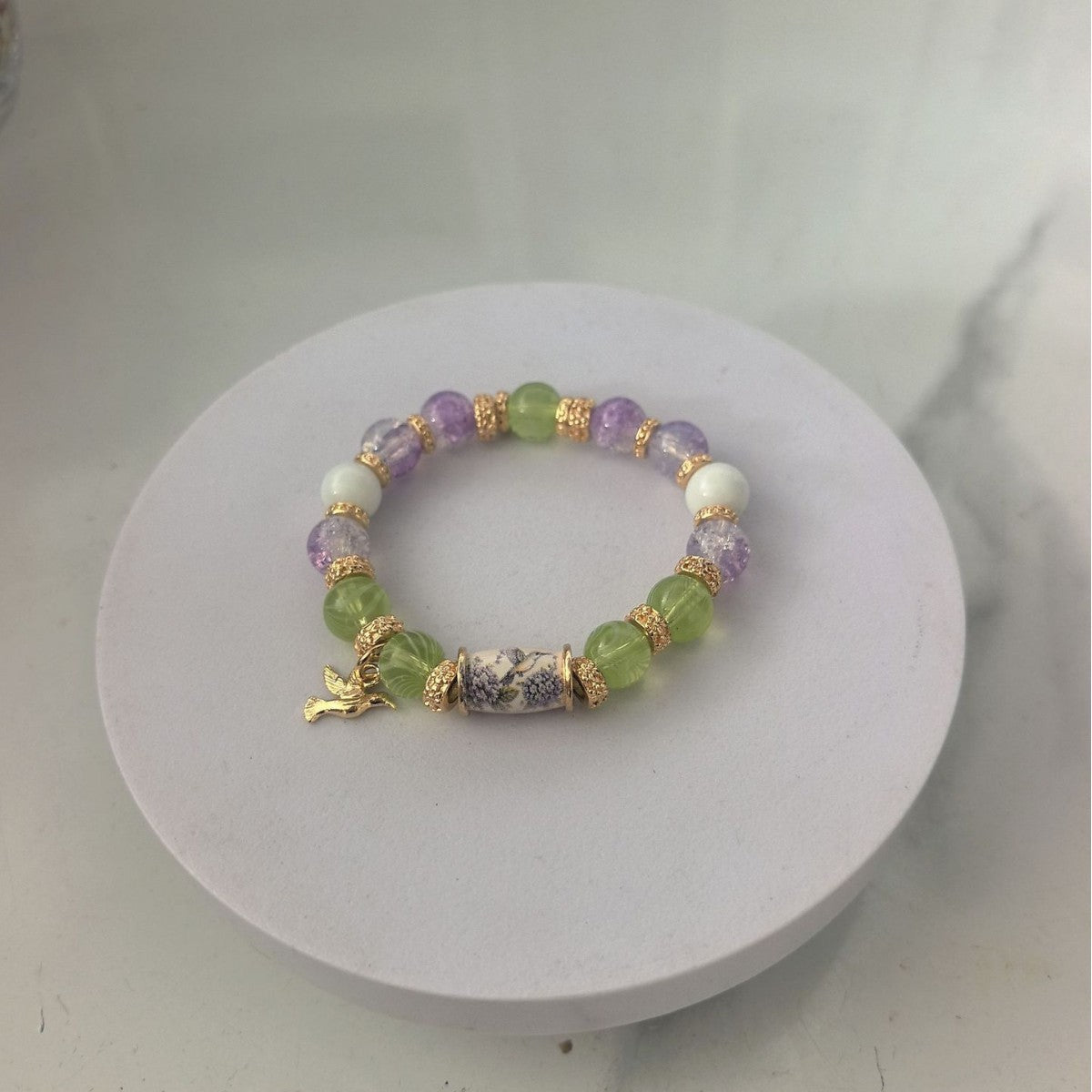 Beaded bracelet with purple, green, and gold beads and a gold bird charm