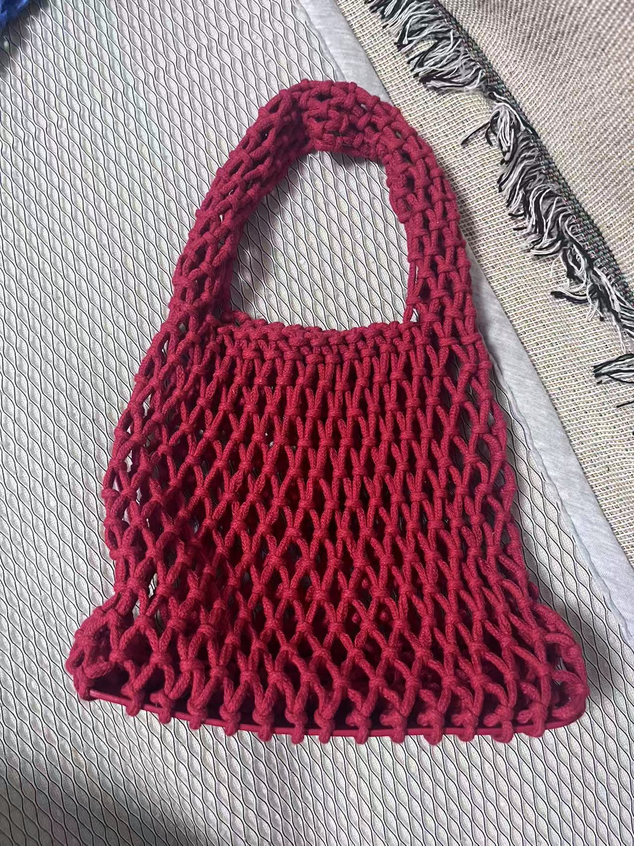 Burgundy woven cotton rope bucket bag with hollow net weave and curved top handle