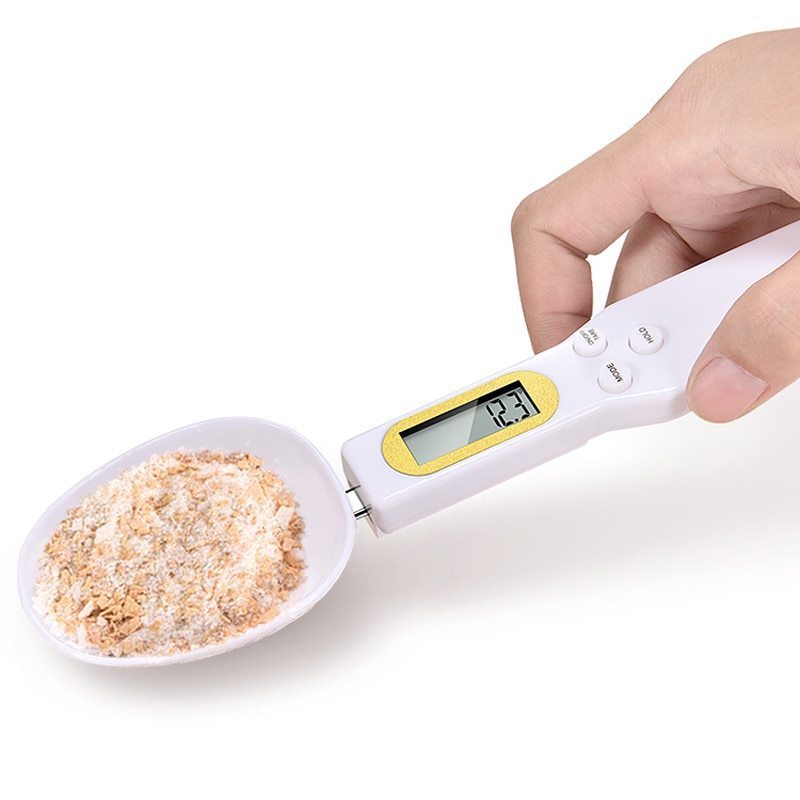 White digital weighing spoon scale with LCD display, held in hand