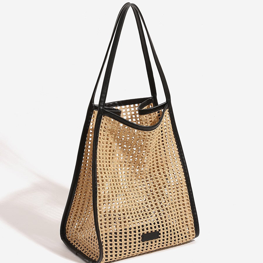 Large woven straw tote bag with black handles, open top, front patch detail
