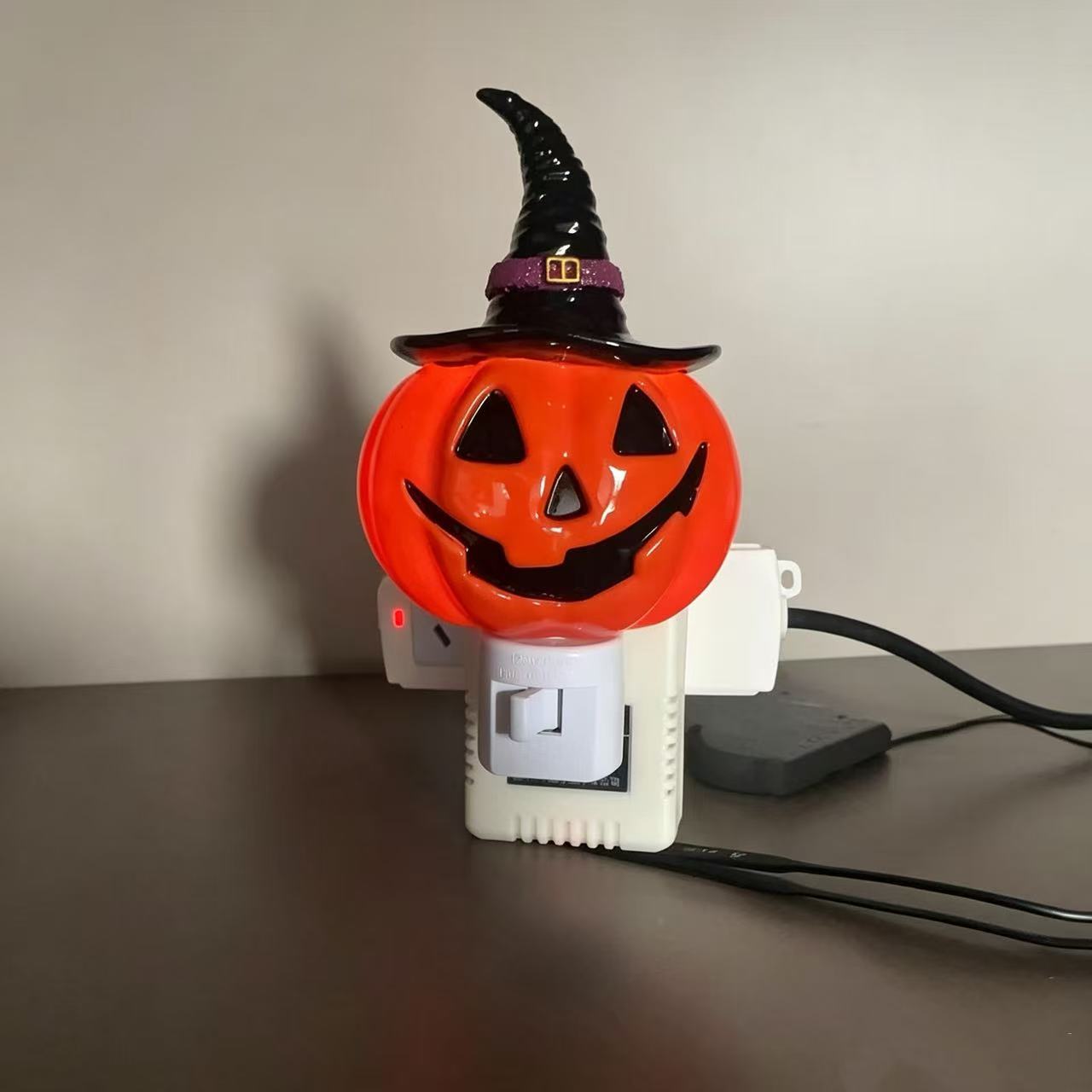 Orange jack-o’-lantern night light with black witch hat and warm glow, wall plug