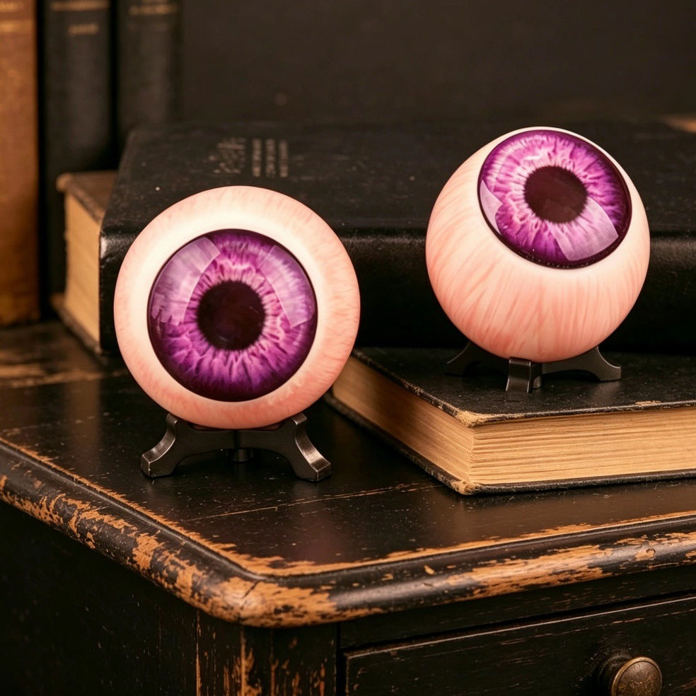 Resin purple eyeball ornament with violet iris on black tripod stand