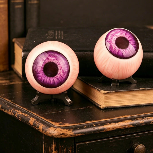Resin purple eyeball ornament with violet iris on black tripod stand