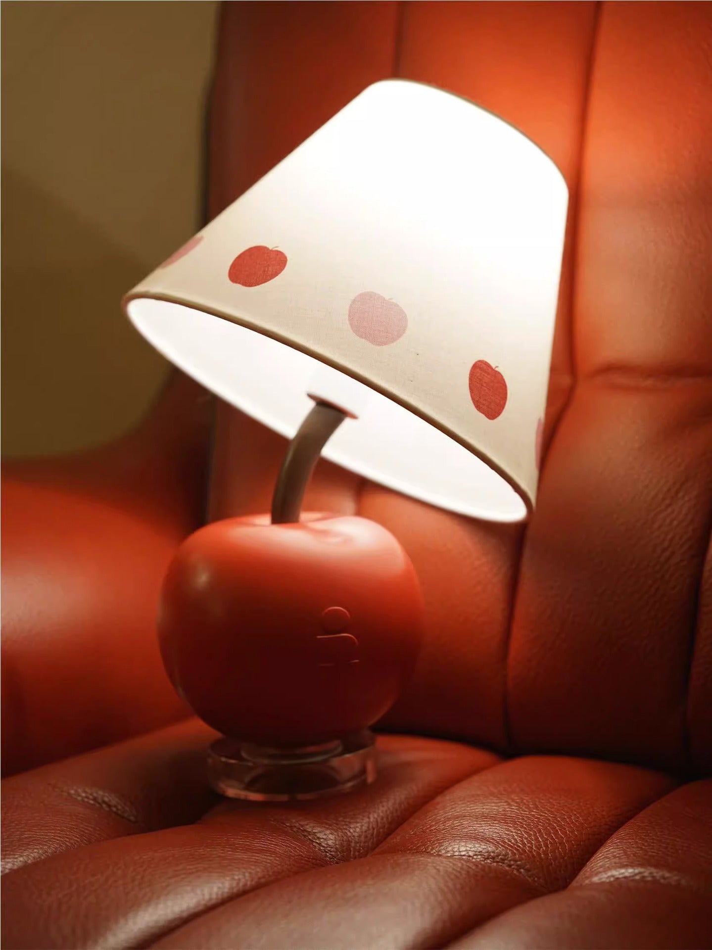 Apple-shaped lamp on sofa with white shade and red heart dots over red base.