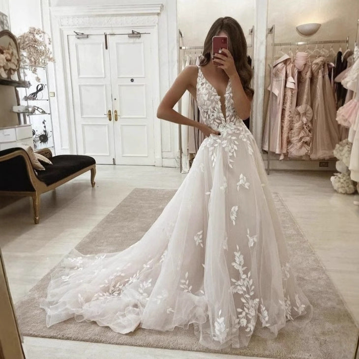 White bridal gown with deep V-neck, floral lace bodice, tulle skirt, and long train.