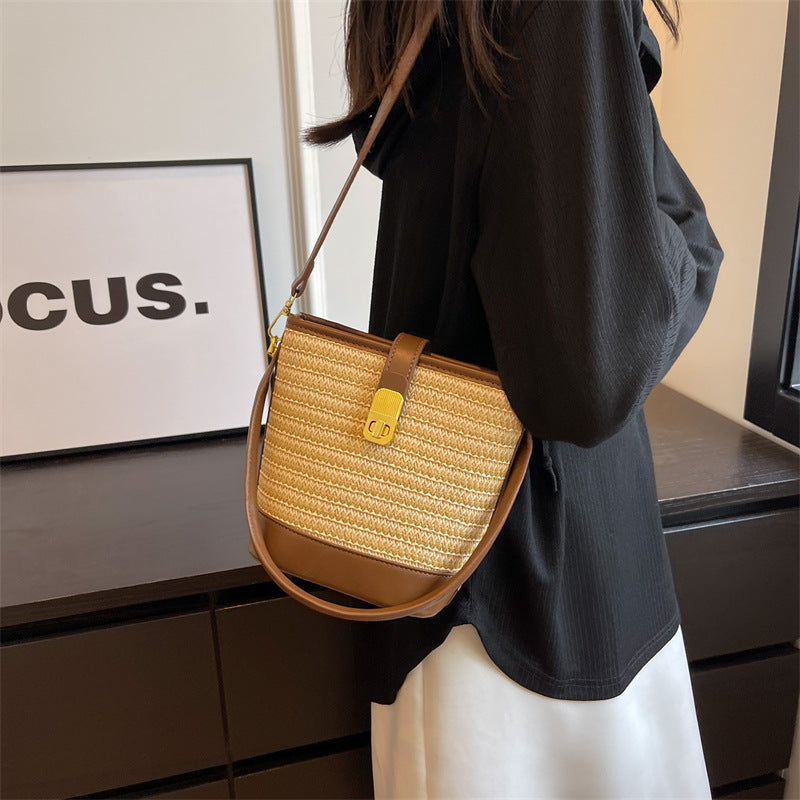 Woven straw bucket bag with tan leather top handle, gold buckle, and shoulder strap.