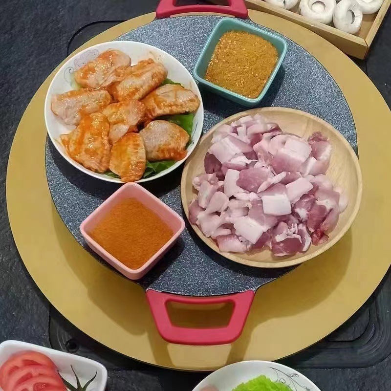Round electric non-stick baking tray with red handles, cooking surface with grilled foods