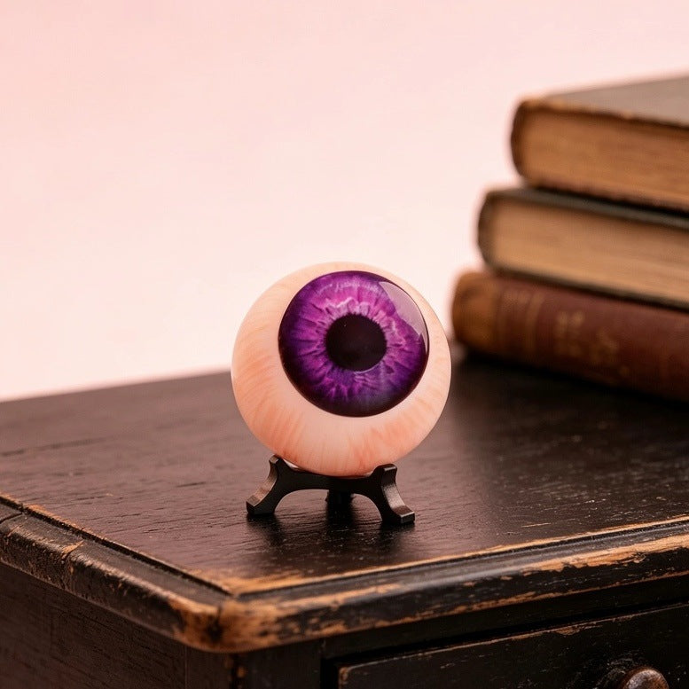 Resin purple eyeball ornament, close view, violet iris on black tripod stand
