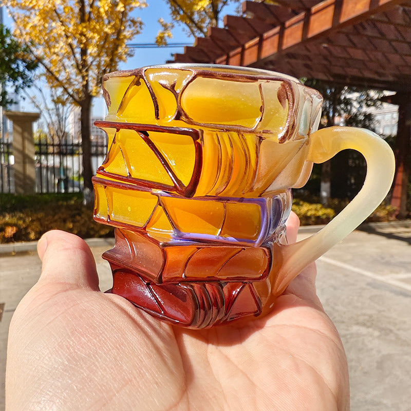 Amber and blue resin book-stack mug in hand, curved handle visible.