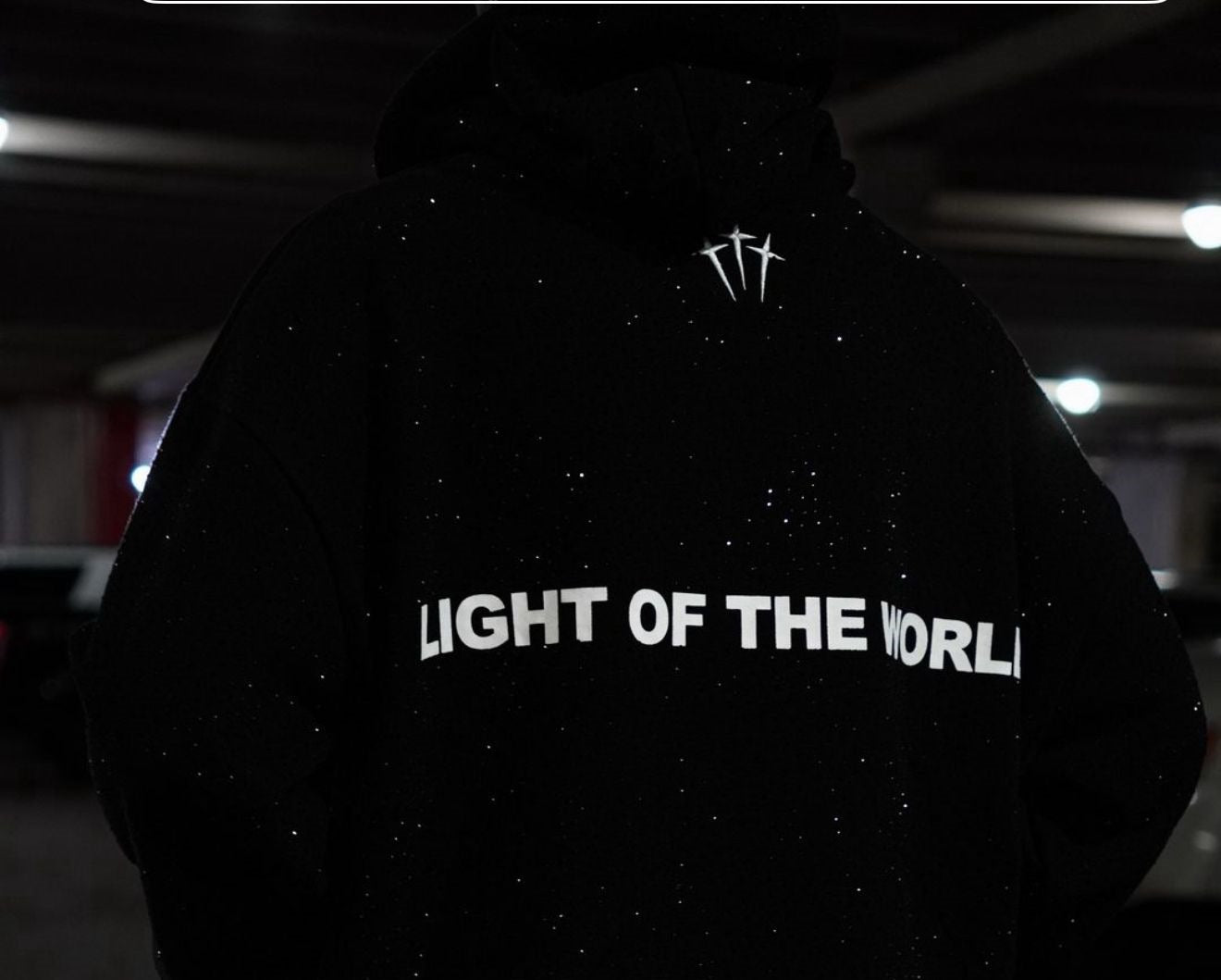 Black pullover hoodie back view with white “LIGHT OF THE WORLD” text and small cross logo