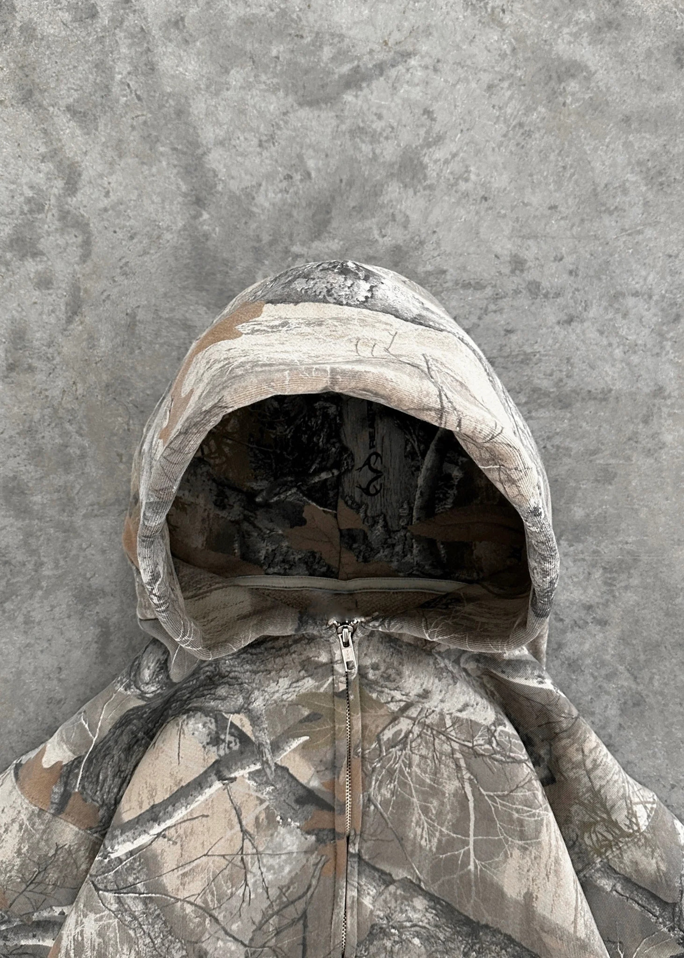 Camouflage hoodie hood with black inner lining and front zipper pull, gray tan print